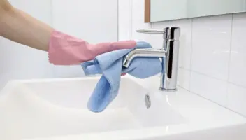 Woman cleaning hard water stain off the faucet with microfiber cloth and gloves