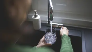 Close up of a senior woman's hand filling a glass of filtered water from the kitchen sink tap. Cost of a water softener